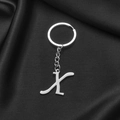 Polished silver stainless steel letter X keychain pendant on black silk fabric background - Letter X