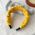 Elegant yellow velvet pleated headband with soft texture on a white plush surface - Yellow
