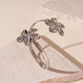 Primer plano detallado de un brazalete de flor plateado pulido sobre piedra crema - Brazalete-Flor Plateada