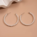Primer plano de aretes de aro de perlas elegantes sobre un fondo marrón cálido de estilo minimalista - Aro grande con perlas pequeñas