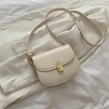 Minimalist cream white saddle bag with golden clasp over a beige blazer - White