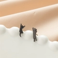 Detailed view of asymmetric black cat silhouette stud earrings on white ceramic tray - 756 Black