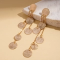 Detailed view of layered gold tassel earrings with textured round metal discs on marble - Gold