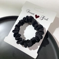 Minimalist black velvet scrunchie displayed on white card over elegant dark backdrop - Black
