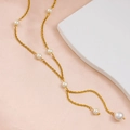 Dettaglio di un'elegante collana lunga dorata a Y con perle bianche su sfondo di seta - Collana