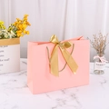 Pink paper gift bag featuring a large gold silk bow and matching woven rope handles - Pink