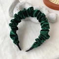 Fashionable dark green velvet headband with pleated design shown on a soft white carpet - Green