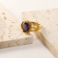Detailed close-up of 18K gold-plated ring with a round purple gemstone on travertine stone - Gold Purple Zirconia