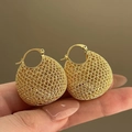 Macrodetail van goudkleurige geweven holle mesh-oorbellen met een complexe textuur - Creolen Sluiting Stijl / Goud