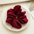 Detail of premium burgundy satin scrunchie with silver logo tag on a ceramic plate - Dark Red
