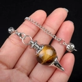 Tiger eye crystal pendulum necklace with metal chain held against a dark background - Tiger's Eye