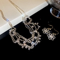 Vue détaillée des boucles d'oreilles fleurs dorées et du collier à strass multicouche - Doré