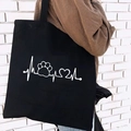 Black canvas tote bag featuring white heartbeat dog paw print and heart graphic design - Pet Heartbeat Print