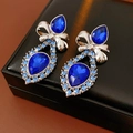 Detalle de pendientes de lazo plateados con cristales azules sobre un estuche de cuero - Pendientes de gota de agua con lazo y aguja de plata - Plata