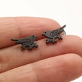 Close-up of matte black bird on branch stud earrings held on a finger for size - Black