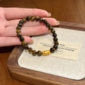 Detail van tijgeroog kralenarmband met een gouden dierenkop bedel vastgehouden - Armband-Goud-Bruin (Tijgeroog Kralen met Kattenbedel)