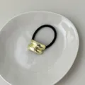 Minimalist elastic hair tie with a wavy gold metal buckle on a white ceramic plate - Asymmetric Smooth Gold