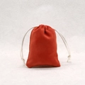 Close-up of a brick red velvet jewelry pouch with white braided drawstring detail - Rust red