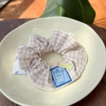 Detailed shot of a beige plaid fabric scrunchie with a blue Notes label in a ceramic bowl - Blue Label - Yellow Pencil Khaki Checkered Scrunchie