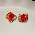 Dettaglio macro di orecchini dorati con pietre rosse quadrate su vassoio in ceramica - Orecchino con perno in argento sterling 925 - Oro - Rosso