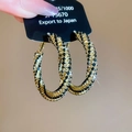 Detailed macro view of spiral gold hoops with black and clear crystals on a black card - Black Gold (Silver Needle)