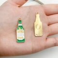 Detail of green enamel beer bottle charms in hand showing actual size and metal texture - Green Enamel Beer Bottle (37x12mm)
