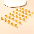 Détail de 24 breloques couronnes dorées pour tresses ethniques sur un fond rose doux - 30Pcs Q930 Anneaux de Tresse Couronne Creuse