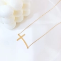 Collana minimalista dorata con ciondolo a croce curva su supporto geometrico bianco - Stile Croce ad Arco