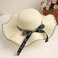 Detailed view of cream straw hat featuring black wavy edge stitching and lettered bow ribbon - White