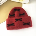Detail of red knit beanie with black velvet bows on a minimalist white table - Burgundy