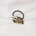 Detailed macro view of a golden leaf metal hair tie with a black elastic band on white fabric - Leaf Shape (5) / Gold