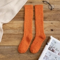 Thick orange coral fleece knee-high socks laid on a rustic wooden background - Orange