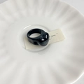 Nahaufnahme eines polierten schwarzen Herzrings aus Harz auf einer weißen Keramikschale - Stil B Glänzend Schwarzes Herz Ring (X-254)
