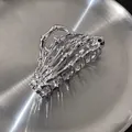 Macro shot of silver bone-shaped metal hair claw clip on a brushed metal tray - Skeleton Hand Claw / Silver