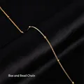 Macro shot of gold-plated titanium box chain with metal beads on black silk fabric - Box Chain with Beads / Gold