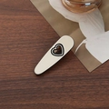 Chic cream-colored oval hair claw clip featuring a black heart motif on a wooden surface - Heart Shape Duckbill Clip / Beige