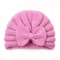 Close-up of pink knitted baby hat featuring a large decorative bow and soft yarn texture - Pink