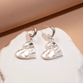 Vista dettagliata degli orecchini a cuore in argento con finitura martellata elegante - Cuore Piegazzato (Perno in Argento - Argento - Cuore Piegazzato)