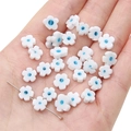 Flat plum blossom lampwork beads in white and blue held in palm for size reference - White with Blue Dots