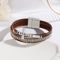 Close-up of brown leather multilayer bracelet with rhinestones and blessed cross charm - Brown