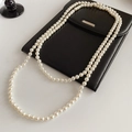 Long collier de perles blanches élégamment drapé sur une pochette en cuir noir - Collier-Blanc