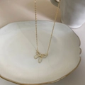 Detailed view of a gold bow pendant necklace with zircons resting on a ceramic plate - Bow