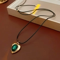 Détail d'un collier cœur vintage avec pendentif gemme verte et bordure dorée - Vert