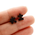 Close-up of matte black puzzle piece stud earrings held to show relative scale - Jigsaw Puzzle / Black