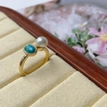 Detail of a gold ring featuring a lustrous white pearl and oval green turquoise stone - Turquoise Gold