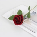 Lifelike single red velvet artificial rose with green leaves on an open magazine - Small Velvet Wine Red