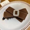 Detail of a dark brown velvet bow hair clip with a sparkling rhinestone buckle on a ceramic plate - Brown