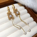 Dettaglio di orecchini a forma di orsetto con perle pendenti e nappe dorate su velluto - Marrone