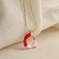 Gros plan du pendentif lettre A doré avec émail rouge et rose sur tissu beige - Style-Q