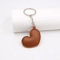 Llavero minimalista de cuero PU marrón con forma de corazón y costuras sobre blanco - café